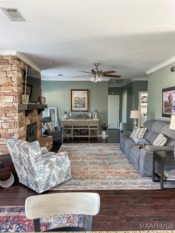 living room with crown molding, visible vents, wood finished floors, and a stone fireplace