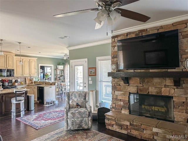 living room with ornamental molding, dark wood-style flooring, ceiling fan, and a stone fireplace