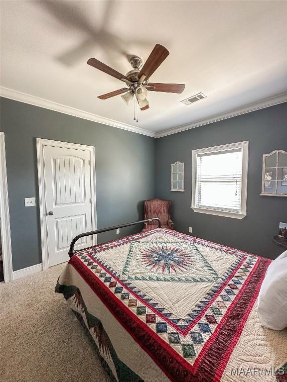 carpeted bedroom with ceiling fan, baseboards, visible vents, and crown molding