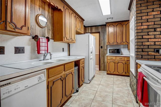 kitchen featuring white appliances, brown cabinetry, light countertops, a sink, and light tile patterned flooring