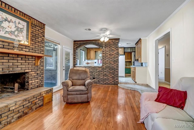 living area featuring visible vents, a ceiling fan, light wood-style flooring, ornamental molding, and a fireplace