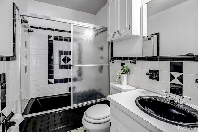 bathroom featuring bath / shower combo with glass door, vanity, toilet, and tile walls