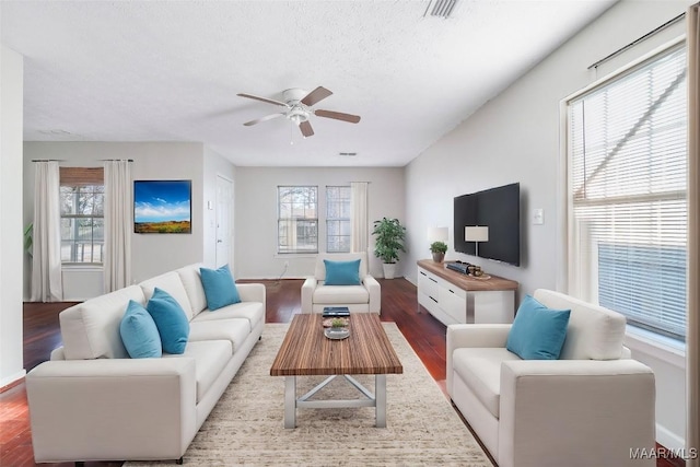 living area featuring a textured ceiling, wood finished floors, visible vents, a ceiling fan, and baseboards