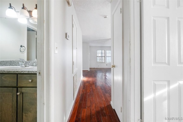 hallway with dark wood-style flooring, a sink, visible vents, and baseboards