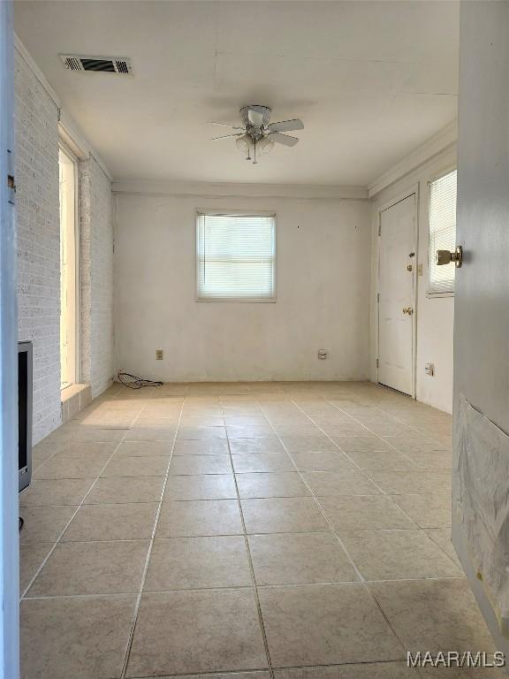 spare room featuring crown molding, a fireplace, light tile patterned floors, visible vents, and a ceiling fan