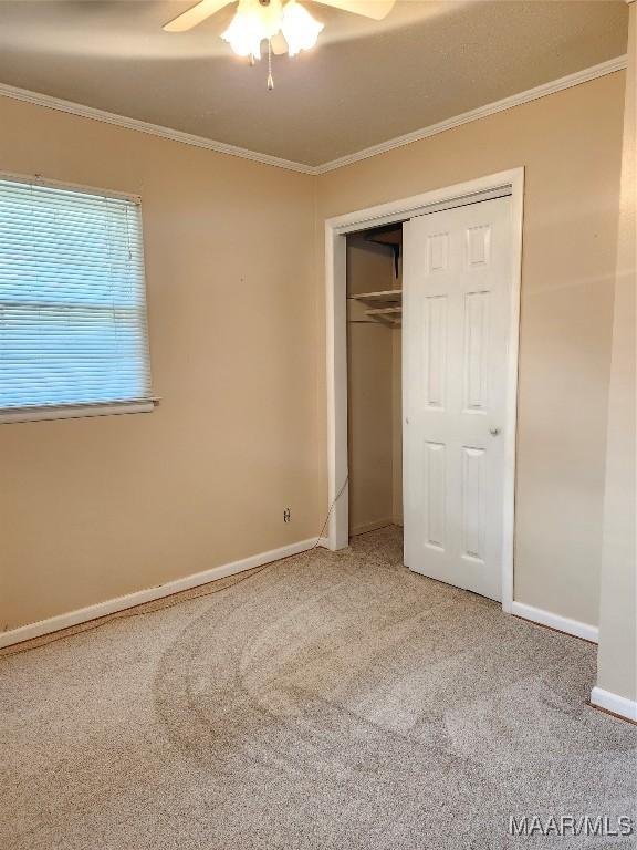 unfurnished bedroom with a ceiling fan, baseboards, ornamental molding, a closet, and carpet