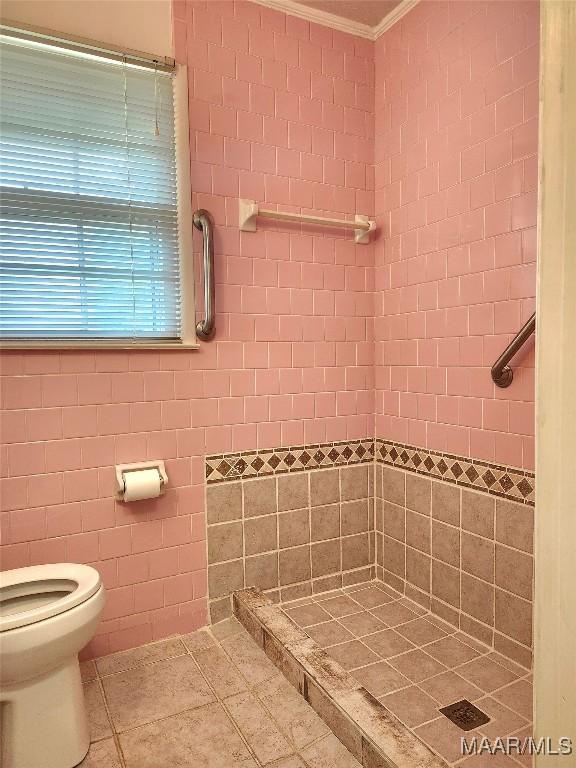 bathroom featuring toilet, tile patterned flooring, crown molding, and a shower stall