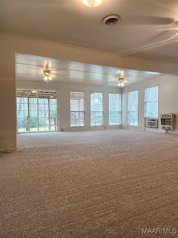 carpeted spare room featuring heating unit, a healthy amount of sunlight, ceiling fan, and visible vents