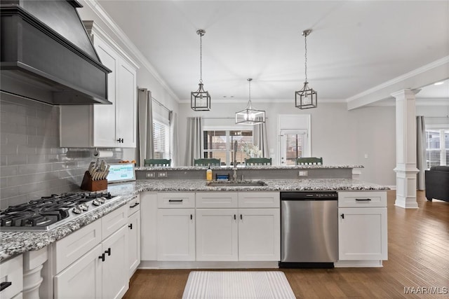 kitchen with a sink, white cabinets, appliances with stainless steel finishes, custom exhaust hood, and ornate columns