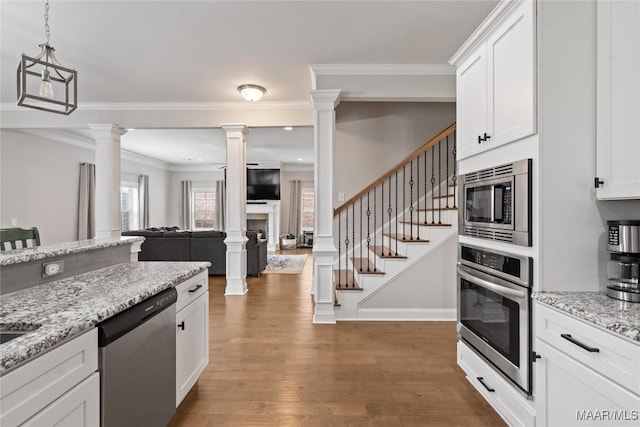 kitchen featuring wood finished floors, stainless steel appliances, ornate columns, a fireplace, and white cabinetry