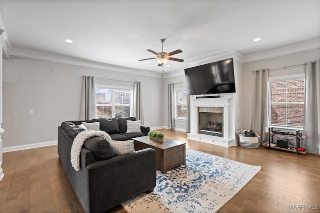 living room featuring baseboards, a fireplace with raised hearth, hardwood / wood-style flooring, and crown molding