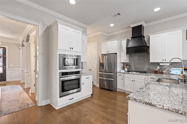 kitchen with wood finished floors, a sink, visible vents, appliances with stainless steel finishes, and custom range hood