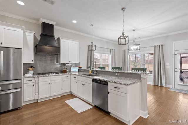 kitchen with custom range hood, a peninsula, stainless steel appliances, white cabinetry, and a sink