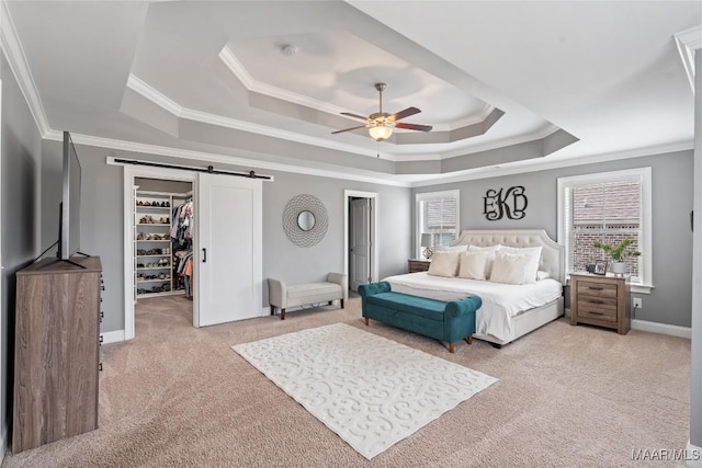 carpeted bedroom with a barn door, baseboards, ornamental molding, a tray ceiling, and a walk in closet