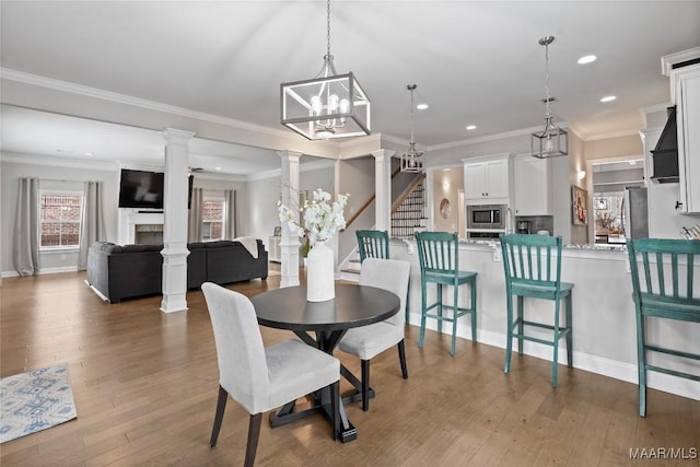 dining room featuring ornate columns, stairs, a fireplace, and wood finished floors