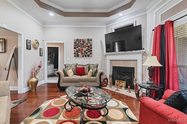 living room featuring crown molding, a raised ceiling, a tiled fireplace, wood finished floors, and baseboards