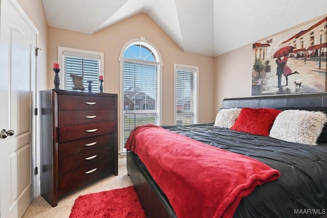 bedroom with vaulted ceiling, a textured ceiling, and light colored carpet