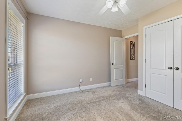 unfurnished bedroom with carpet, a closet, a ceiling fan, a textured ceiling, and baseboards