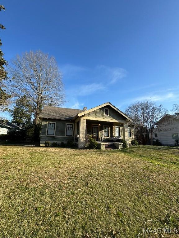 view of front facade featuring a front lawn, a chimney, and a porch