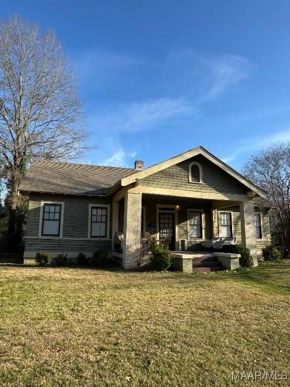 view of front facade featuring covered porch, a front lawn, and a chimney