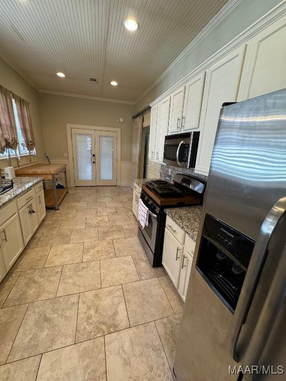 kitchen with stainless steel appliances, white cabinetry, french doors, light stone countertops, and crown molding