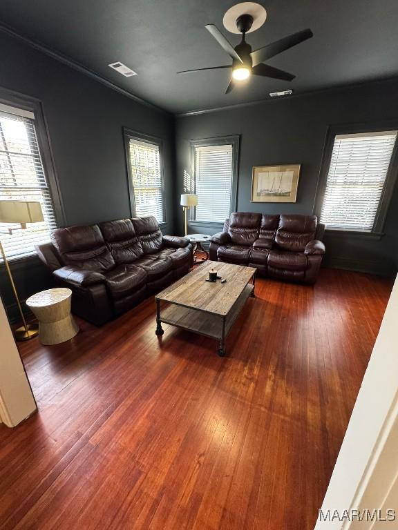 living room featuring dark wood-style floors, visible vents, crown molding, and a ceiling fan