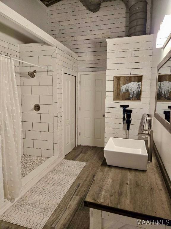 bathroom with tiled shower, a sink, and wood finished floors