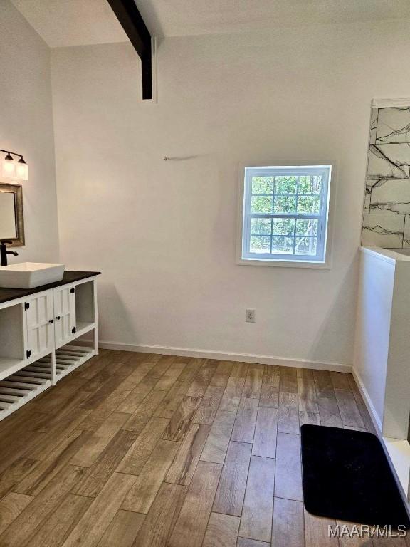 interior space with lofted ceiling with beams, wood finished floors, vanity, and baseboards