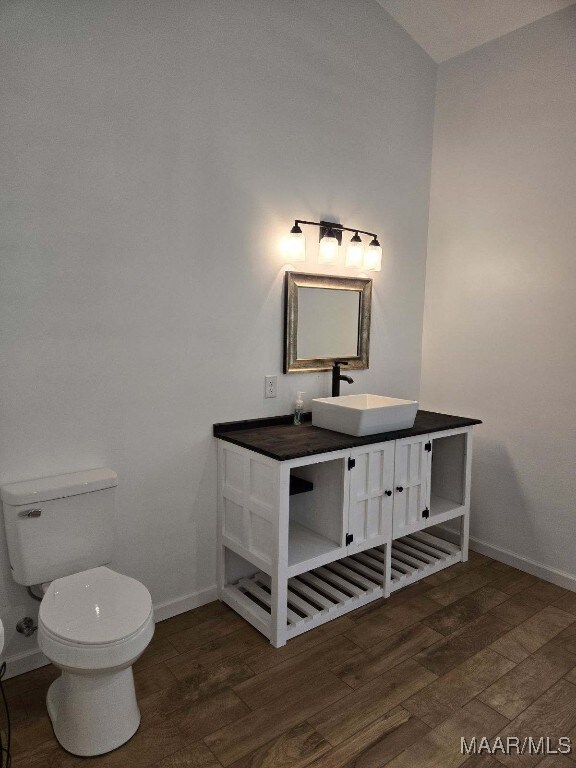 half bath featuring vanity, wood finished floors, toilet, and baseboards