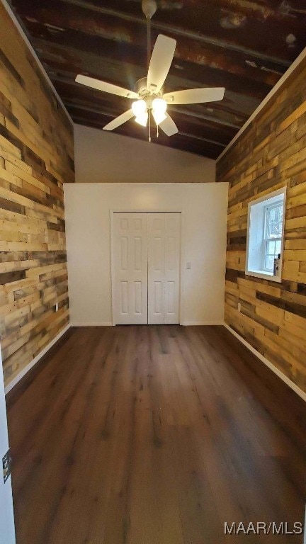 unfurnished bedroom with a closet, dark wood-style flooring, wooden walls, and lofted ceiling with beams