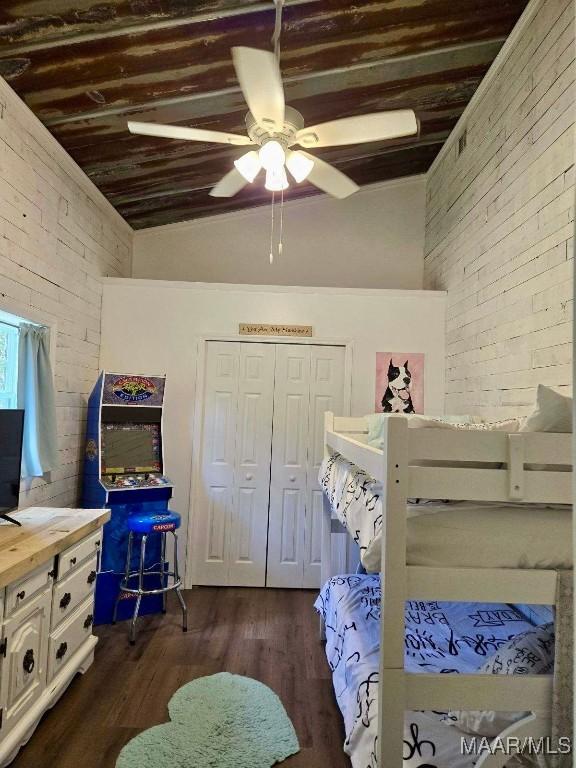 bedroom with a ceiling fan, lofted ceiling, brick wall, dark wood-style flooring, and a closet