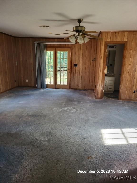 empty room with carpet floors, wood walls, and visible vents