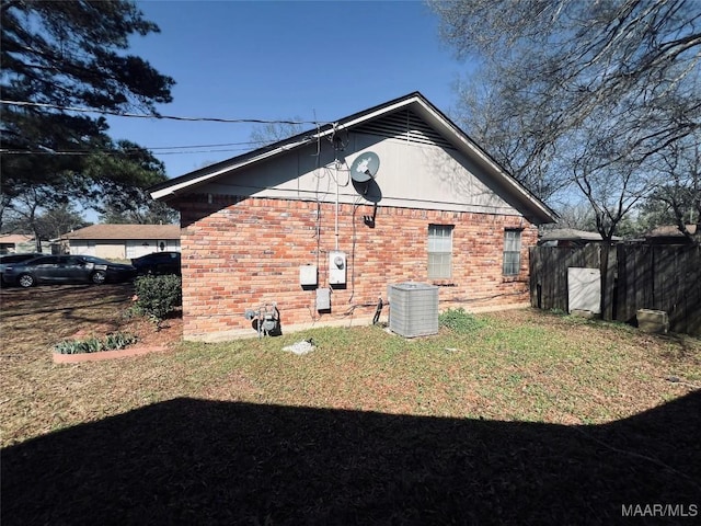 view of side of home with fence, a lawn, cooling unit, and brick siding