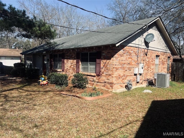 view of home's exterior with a shingled roof, central AC unit, a lawn, and brick siding