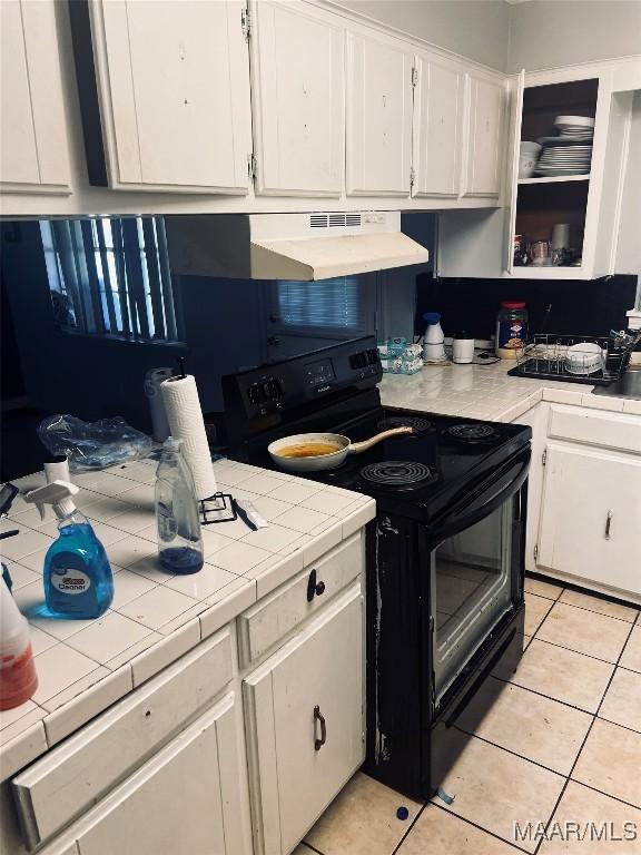 kitchen featuring tile countertops, light tile patterned floors, black range with electric stovetop, white cabinets, and ventilation hood