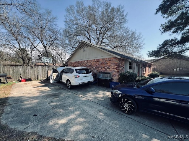 view of property exterior featuring concrete driveway, brick siding, and fence