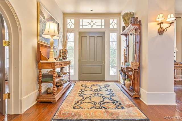 entryway featuring arched walkways, wood-type flooring, and baseboards