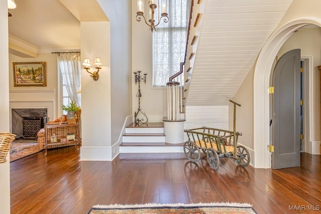 entryway with arched walkways, hardwood / wood-style flooring, a fireplace, stairway, and crown molding