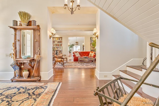 entrance foyer with a notable chandelier, hardwood / wood-style floors, vaulted ceiling, baseboards, and stairs