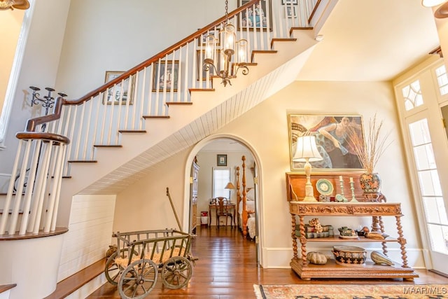 staircase with wood-type flooring, a high ceiling, arched walkways, and baseboards