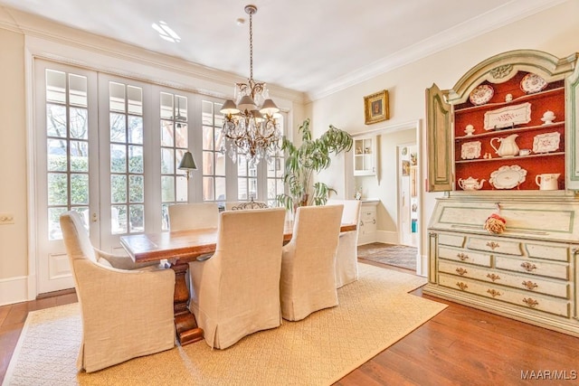 dining area featuring a notable chandelier, baseboards, wood finished floors, and crown molding