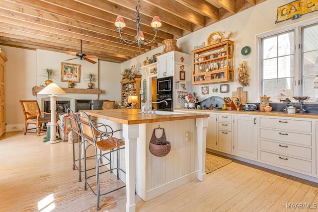 kitchen featuring butcher block counters, black appliances, light wood-type flooring, beamed ceiling, and a kitchen bar