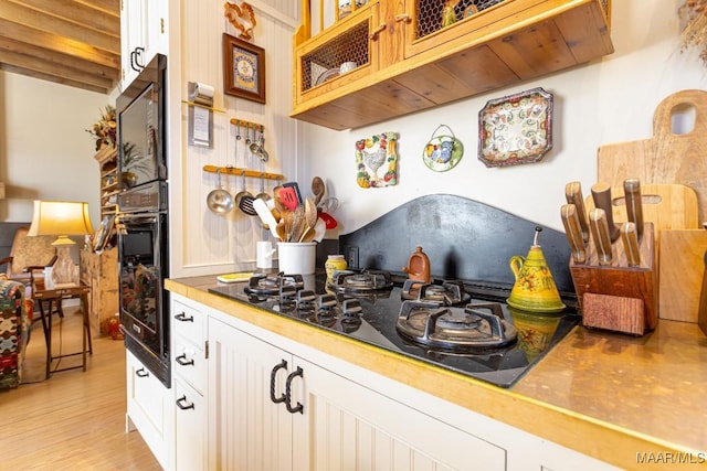 kitchen featuring glass insert cabinets, white cabinetry, light wood finished floors, and black appliances