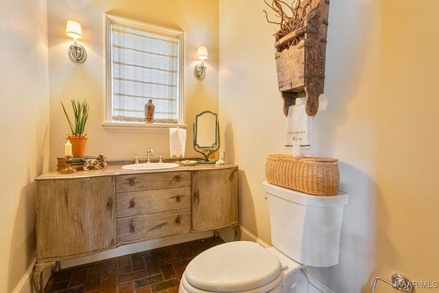 bathroom featuring toilet, brick floor, baseboards, and vanity