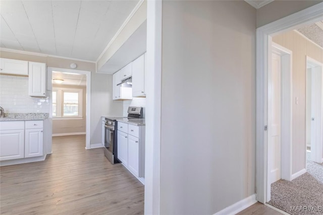 kitchen with electric range, crown molding, under cabinet range hood, white cabinetry, and backsplash