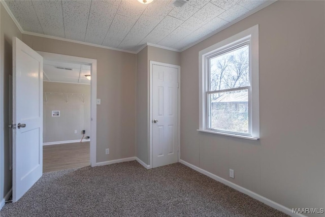 unfurnished bedroom featuring crown molding, a closet, carpet flooring, and baseboards