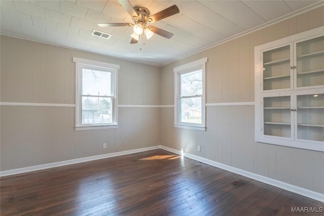 spare room with ceiling fan, wood finished floors, visible vents, baseboards, and ornamental molding