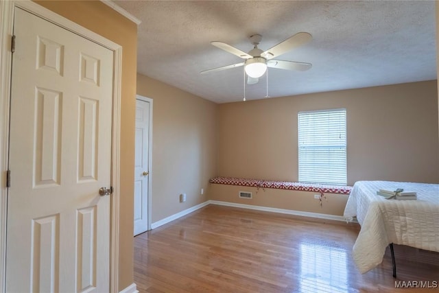 bedroom with visible vents, ceiling fan, a textured ceiling, light wood-type flooring, and baseboards