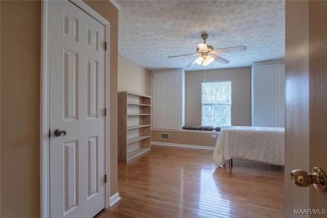 bedroom with baseboards, visible vents, a textured ceiling, and wood finished floors