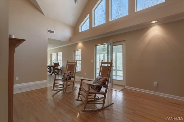 living area featuring high vaulted ceiling, wood finished floors, visible vents, and baseboards